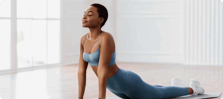 Mulher realizando alongamento no tapete, em postura de extensão, em ambiente claro e minimalista.
